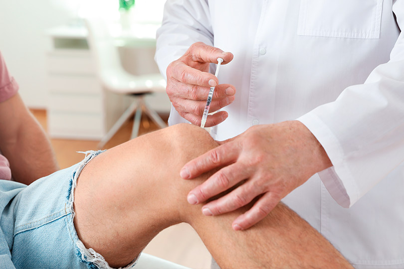 Health professional applying shot at knee. 