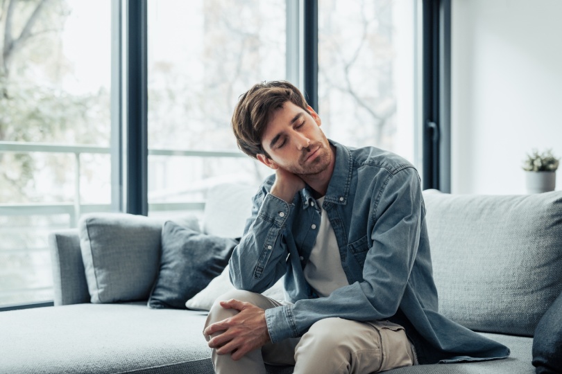 Upset tired young man feeling pain massaging stiff neck rubbing tensed muscles to relieve back ache joint shoulder discomfort after long sedentary work in incorrect posture, fibromyalgia concept