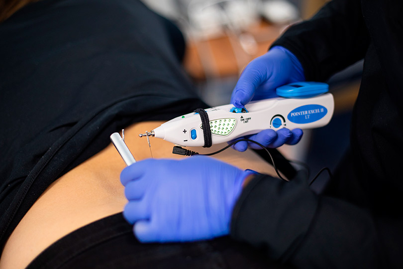 A person using an electric device to perform a skin incision during a pain management procedure.