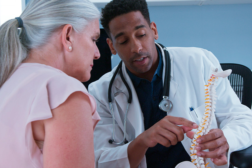  A physician assesses a woman's spine, focusing on spinal cord stimulation treatment for elderly patients.