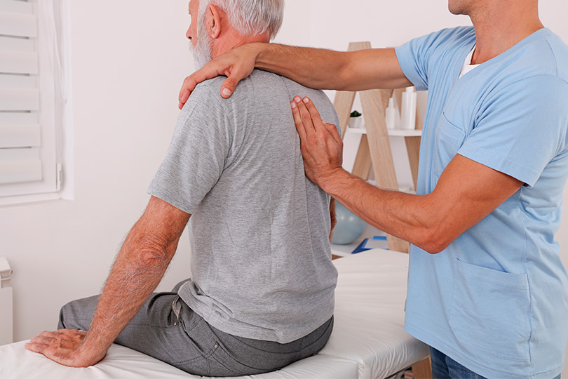 A healthcare professional assesses a senior man's back, addressing spinal cord stimulation therapy.