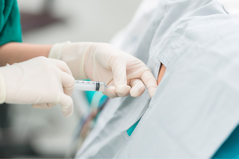 A person in a green shirt holds a syringe, symbolizing the blend of traditional and modern pain treatment methods.