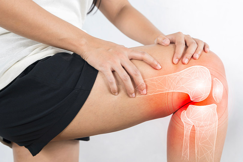 A woman grimacing while rubbing her knee, symbolizing the struggle with knee pain and its effects on mobility.