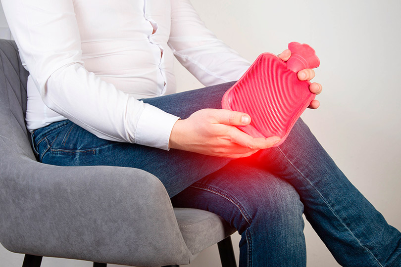 A man seated with a hot water bottle, seeking comfort and relief from winter-related aches and pains.
