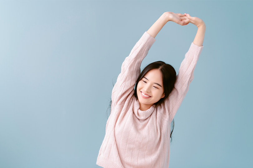 Asian woman reaching her arms high, representing natural approaches to winter weather pain relief.