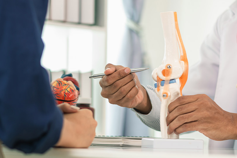 A physician inspects a knee model, focusing on innovative pain management treatments for knee-related conditions.