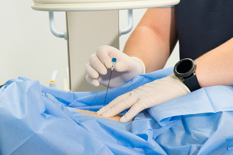 A person in a blue gown receives a needle, possibly for a medical treatment related to neck pain relief in Mission.