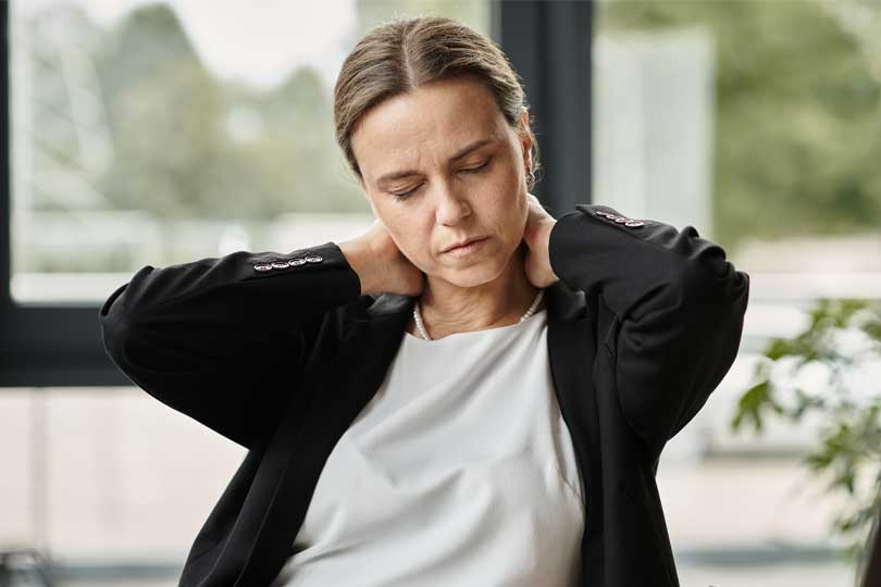 Middle-aged woman with neck pain, stressed, sitting in front of laptop.